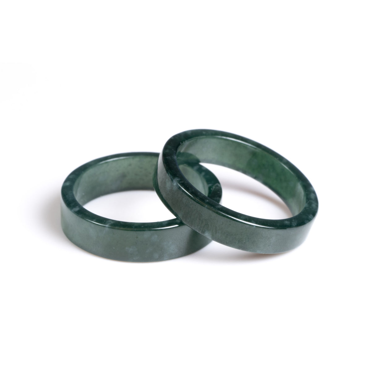 Two natural jade rings in deep green colour positioned on a white background.