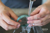 A jade bangle under running water being washed by hand.