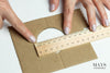 a woman measuring the diameter of a cardboard cutout. mays jade bangle sizing guide.
