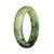 A close-up of a half-moon shaped jade bangle with a vibrant green pattern.